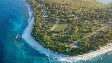 An aerial view of a coastal property with a beach, clear waters, and a mix of residential and undeveloped land.