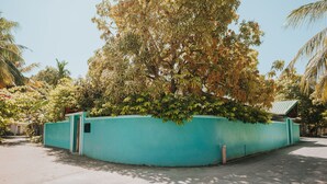 Una pared azul turquesa curvada con un árbol en el centro, rodeada de diversas plantas y árboles.