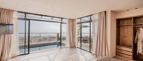 A modern bedroom with a large window, a bed, a wooden wardrobe, and a view of a cityscape.