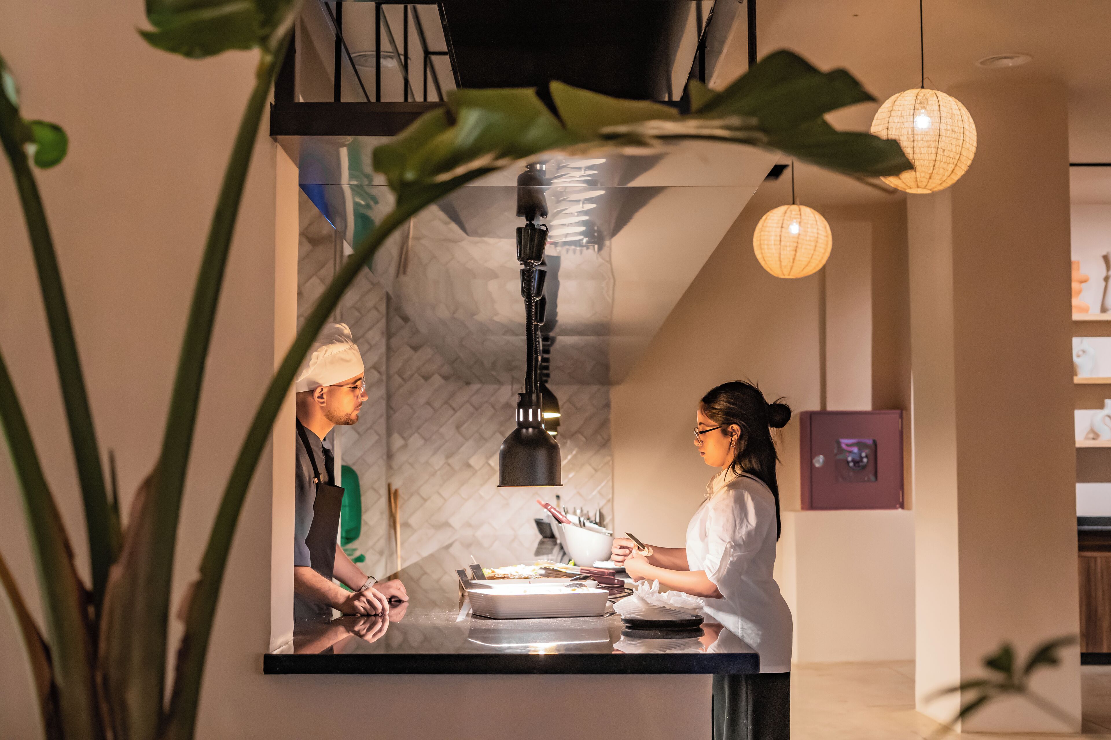 Une cuisine moderne dotée d’un plan de travail en acier inoxydable, de luminaires suspendus et d’un pare-feu apparent.