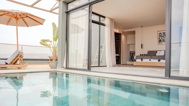 Un espace piscine intérieur moderne, doté de parois en verre transparent, d’un fauteuil de relaxation et d’une plante en pot.