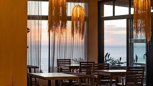 Un espace repas comprenant plusieurs tables et chaises, de grandes fenêtres avec des rideaux et des luminaires sphériques suspendus.