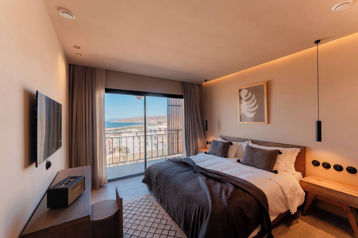 Ein modernes Hotelzimmer mit einem großen Bett, einem Schreibtisch, einem Fernseher und einem Balkon mit Blick auf die Stadt.