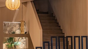 Un escalier moderne aux finitions en bois, flanqué de panneaux géométriques noirs et de pots en terre cuite ornés de plantes.