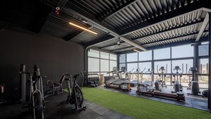 Une salle de sport équipée de divers appareils d’exercice, d’un espace recouvert d’une pelouse artificielle et dotée de grandes fenêtres qui laissent entrer la lumière naturelle.