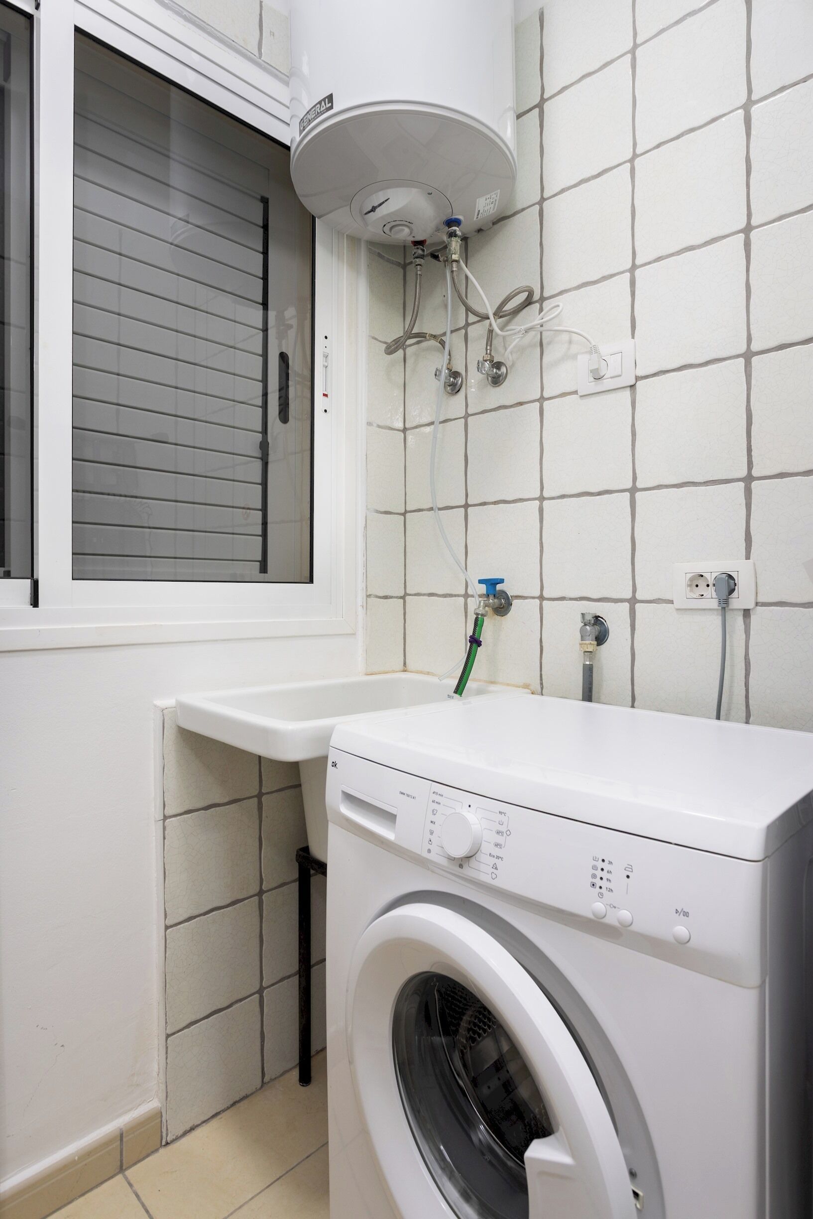 A laundry room with a washing machine, a dryer, a window with blinds, and a water heater on the wall.