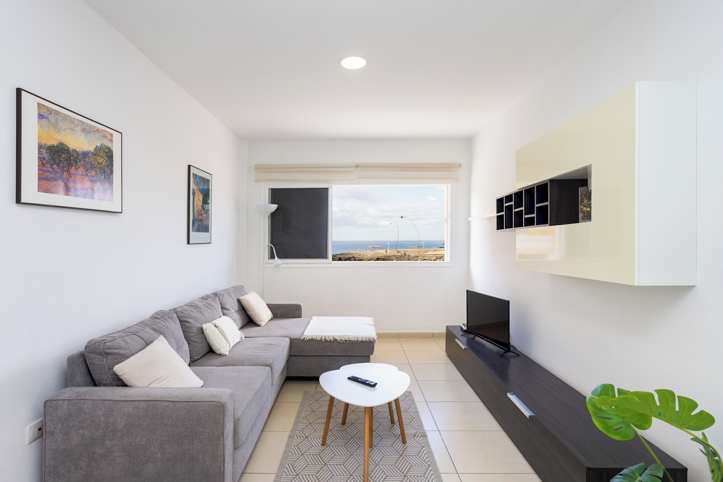 Una sala de estar moderna con un sofá gris, una mesita blanca y un televisor sobre un soporte negro.