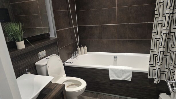 A modern bathroom with a bathtub, toilet, sink, and a mirror. - Apartment - Sleeps 6 & Near Station (Bedford)