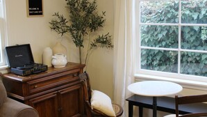 Ein Wohnzimmer mit Holzschrank, Sofa, Tisch und Stühlen. Eine Pflanze, eine Vase und ein Schild sind an der Wand angebracht.