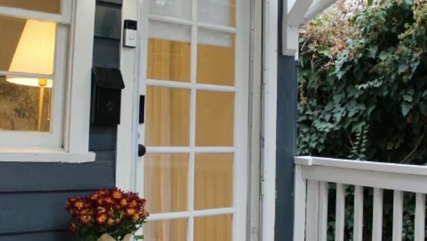 Ein Haus mit weißer Tür, einer kleinen Veranda, einem Blumentopf und einem weißen Geländer.