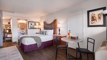 Habitación de hotel con cama, una pequeña mesa redonda con sillas, escritorio, lámpara, espejo y un cuadro en la pared.