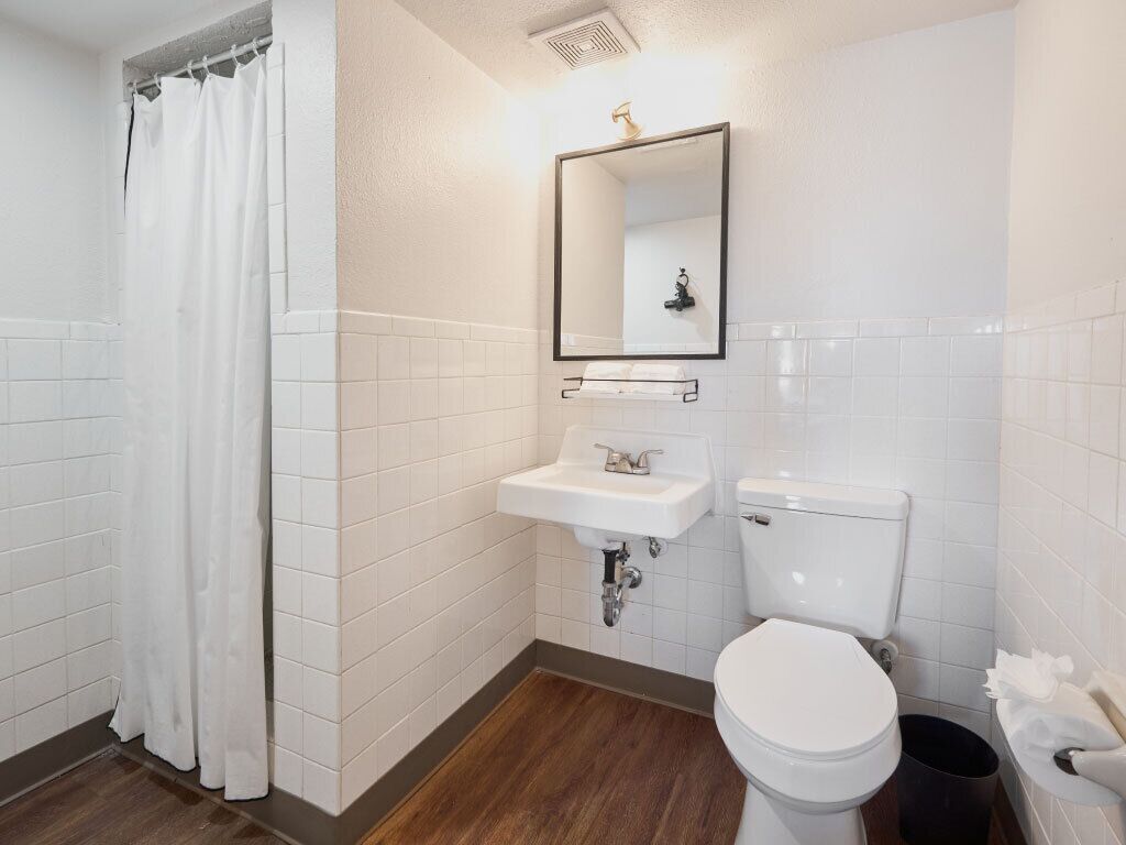 A bathroom with white tiles, a white sink, a toilet, and a shower curtain.