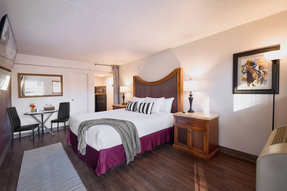 Habitación de hotel con una cama grande, mesitas de noche, escritorio, sillas y vistas al exterior.