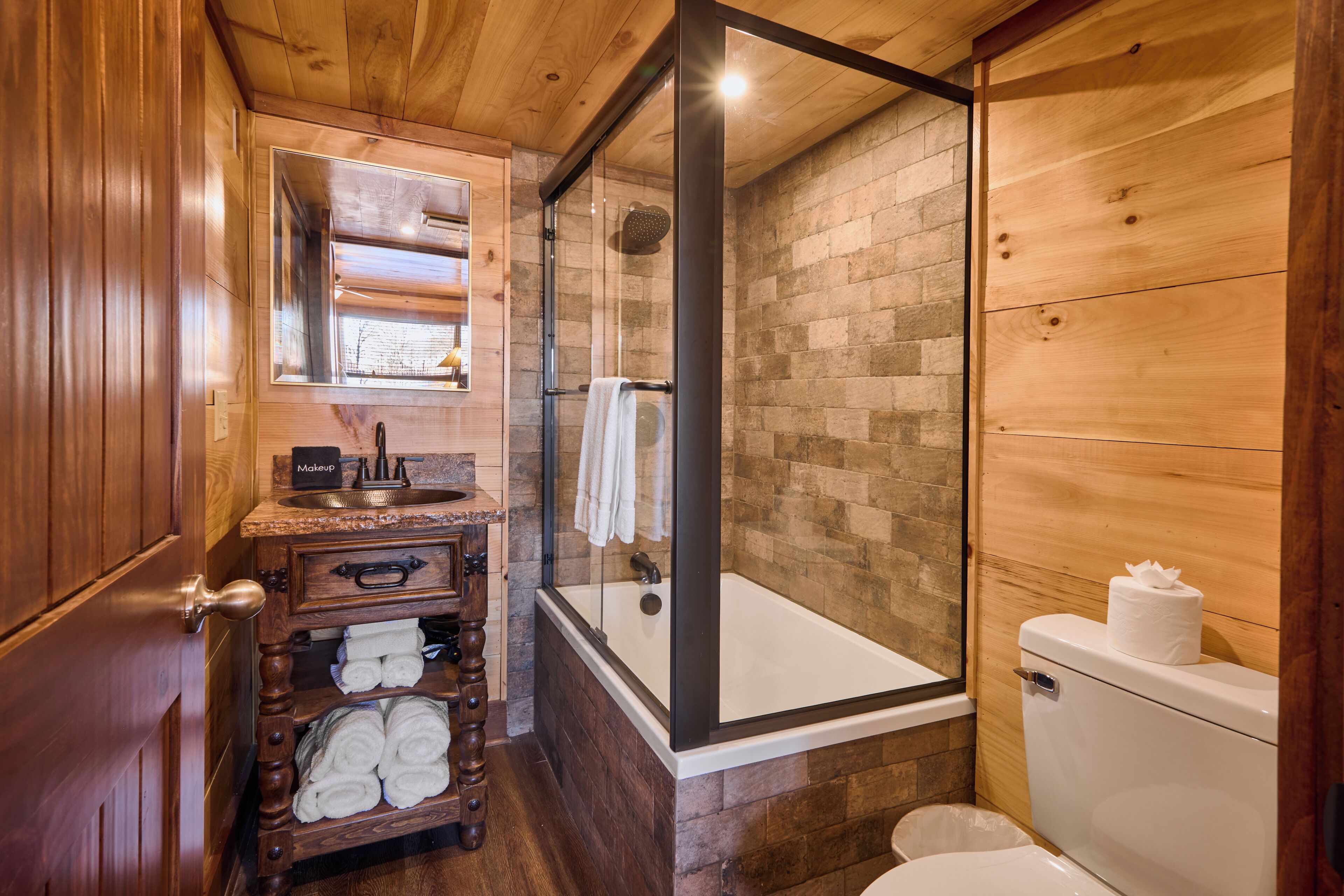 Une salle de bain en bois avec une douche à parois de verre, un lavabo avec un miroir et des toilettes.