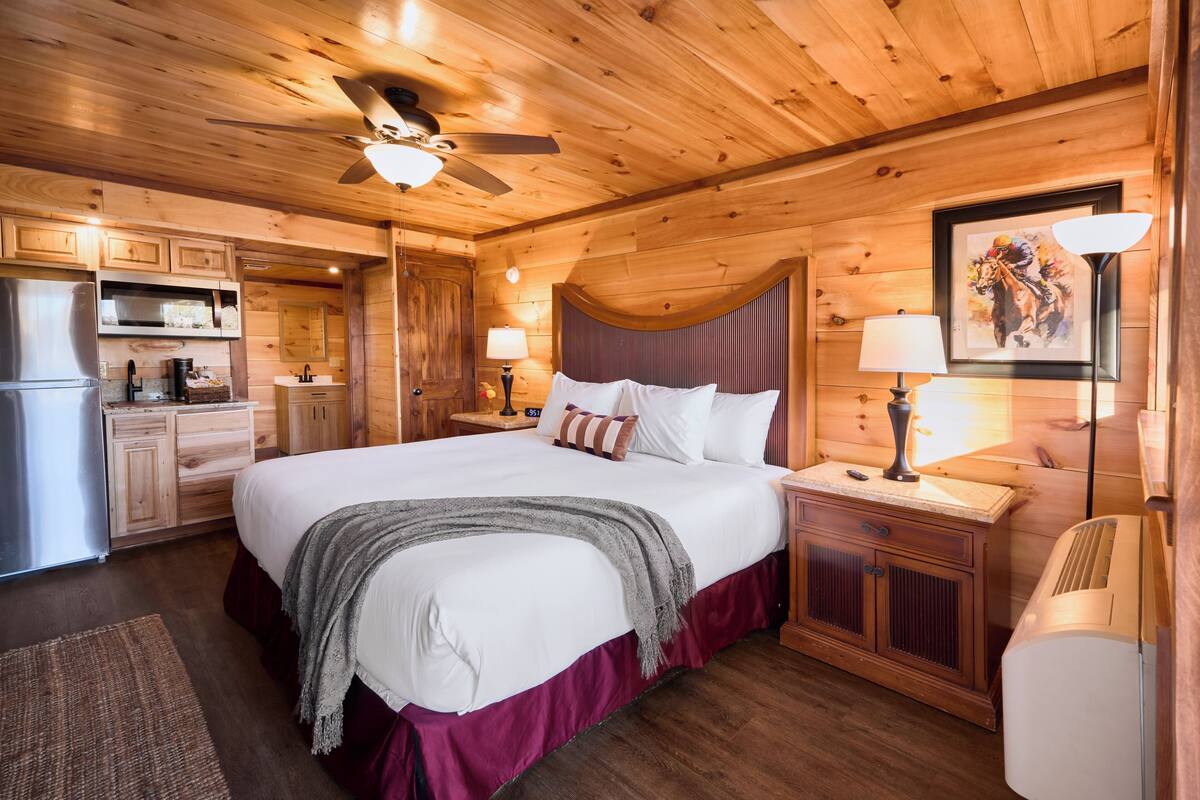 Un dormitorio tipo cabaña de madera con una cama grande, ventilador de techo, refrigerador y un comedor.