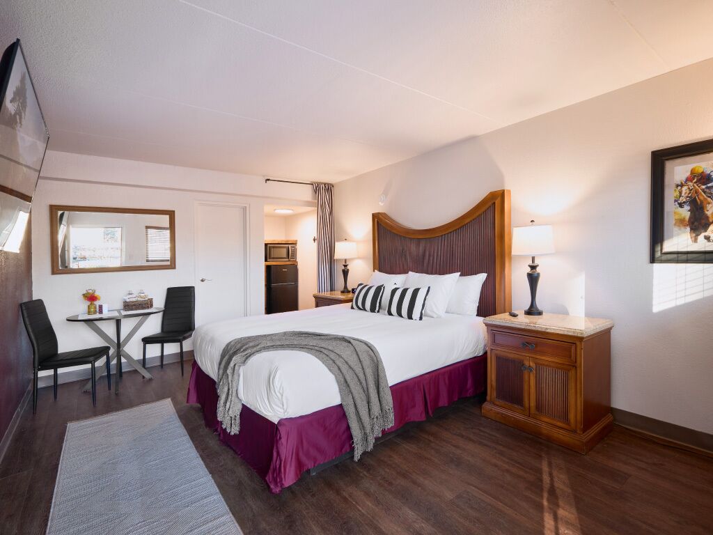 A hotel room with a large bed, a desk, a chair, a nightstand, and a wardrobe.