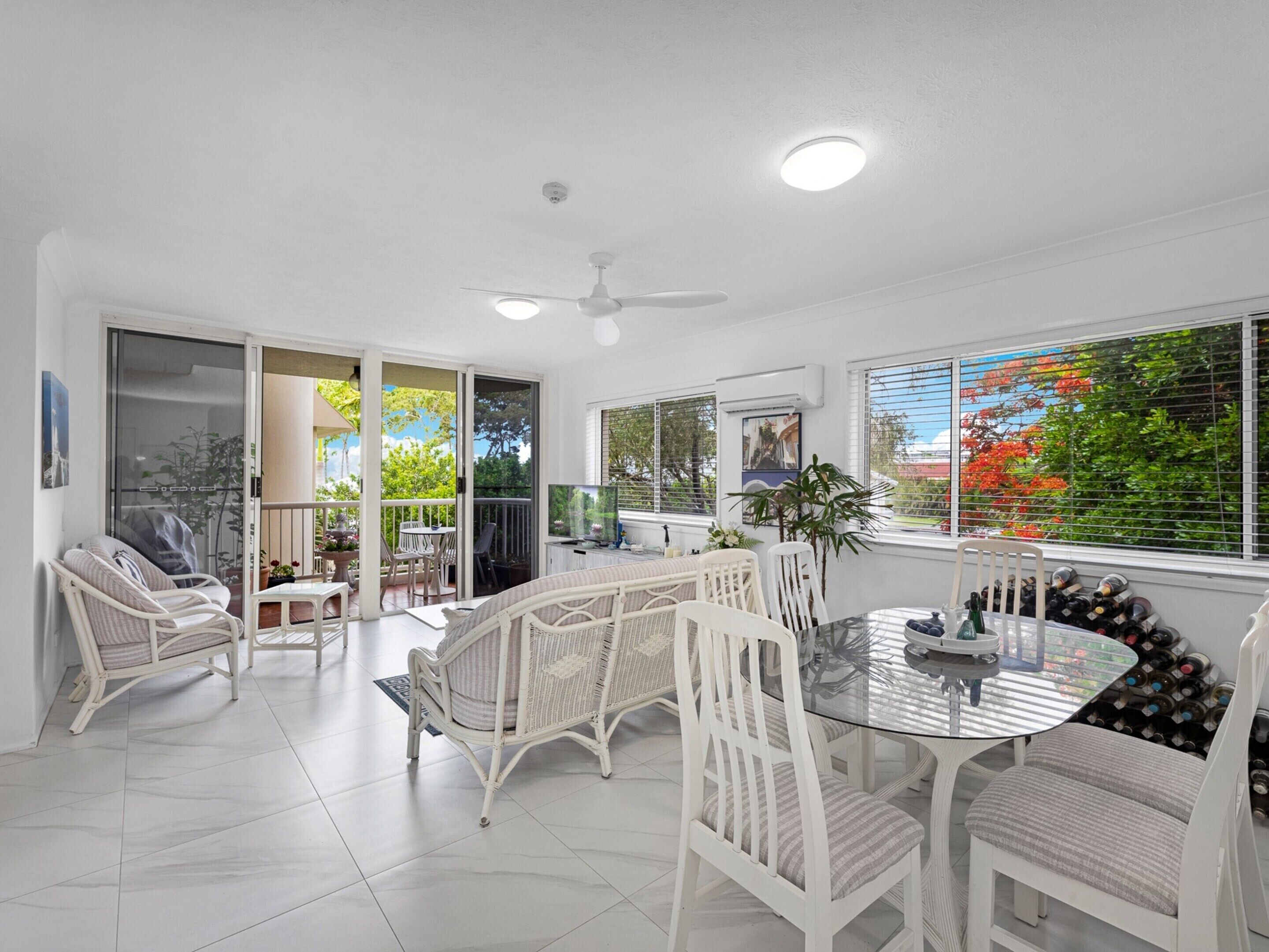 A spacious dining area with a glass table, white wicker chairs, and a ceiling fan.
