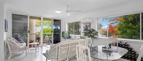 A spacious dining area with a glass table, white wicker chairs, and a ceiling fan.