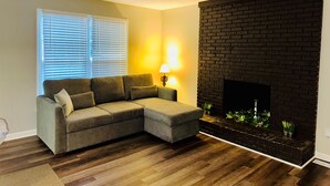 A living room with a sectional sofa, a fireplace, and a lamp. - Midterm 3BR/2BA Rental near Pelham Rd Greenville SC (Greenville)