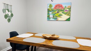 A dining area with a wooden table, four white placemats, a wooden bowl, and a painting of a landscape on the wall. - Midterm 3BR/2BA Rental near Pelham Rd Greenville SC (Greenville)