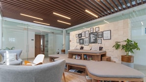 A modern lounge area with a curved bench, grey upholstered chairs, and a wooden bookshelf filled with books. - Rooftop Pool + Hot tub + Gym | Romantic Zone Haven (Puerto Vallarta)