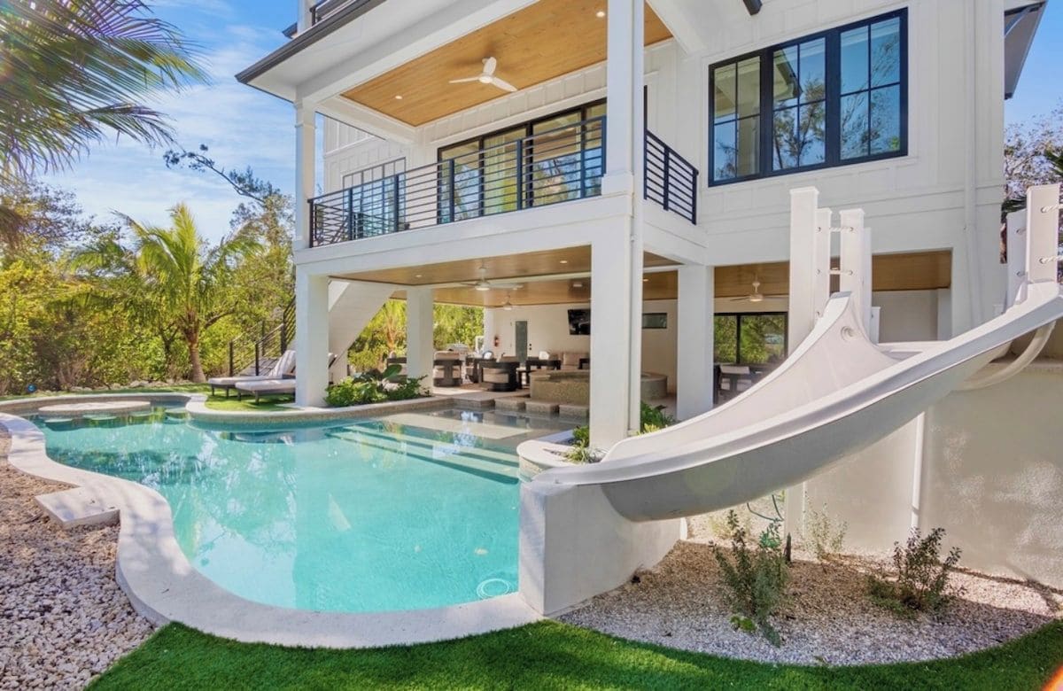 A modern two-story house with a swimming pool, a slide, and a covered outdoor area.