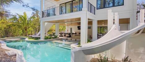 Una casa moderna de dos pisos con piscina, tobogán y un espacio exterior cubierto.