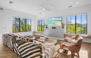A spacious living room with a large TV, comfortable seating, and large windows with a view of the outdoors. - Brand New 9 bedroom house with water slide! (Sarasota)