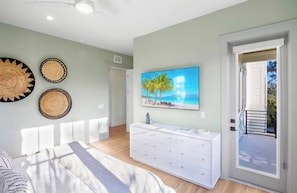 Een slaapkamer met een bed, een witte dressoir, een schilderij van een strandtafereel en een deur naar een balkon.