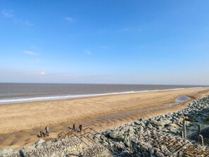 Ein Strand mit felsigem Ufer, blauem Himmel und in der Ferne Windkraftanlagen.