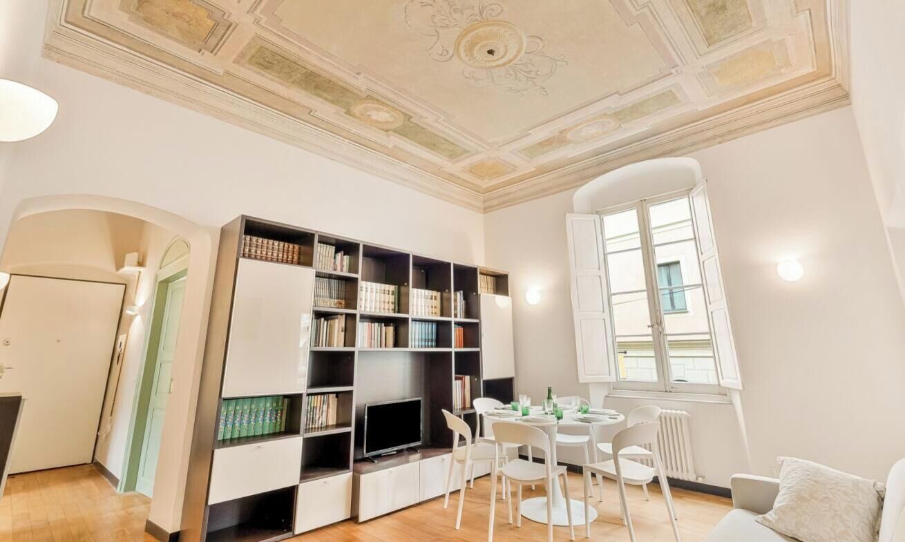 Una stanza con una libreria, un tavolo da pranzo con sedie, una televisione e una finestra con tende.