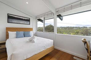 A bedroom with a large bed, a wooden headboard, a view of the countryside through large windows, and a painting on the wall. - Light-filled House Near Beaches and Cafes (Melbourne)