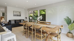 Ein moderner Essbereich mit einem Holztisch und Stühlen, einer schwarzen Couch und einem großen Fenster mit Blick auf Grünflächen.