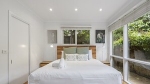 Ein modernes Schlafzimmer mit einem hölzernen Bettgestell, weißer Bettwäsche und Blick auf Grün.