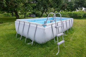 Une piscine hors sol, équipée d’une échelle, entourée de pelouse et d’arbres.