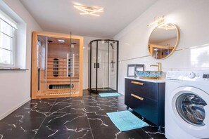 A modern bathroom with a glass-enclosed shower, a wooden vanity, a washing machine, and a large mirror.