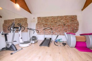 Een huisgym met fitnessapparatuur, waaronder een loopband, een elliptische trainer en gewichten.