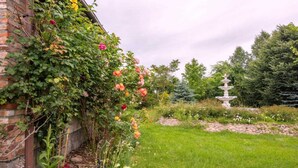 Een tuin met een bakstenen muur, bloeiende planten en een stenen fontein.