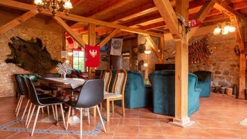Un intérieur rustique avec un plafond en bois, un coin repas comprenant des chaises et une table, et un mur en pierre orné d’un drapeau.
