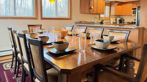 Un comedor con una mesa de madera dispuesta para seis personas, rodeada de sillas. Hay lámparas colgantes sobre la mesa.