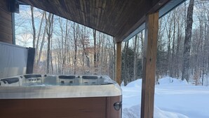 Un jacuzzi bajo una estructura de madera, con un paisaje nevado al fondo.