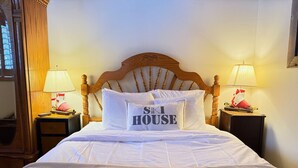 Una cama bien hecha con un cojín que dice "SKI HOUSE" en una habitación de hotel con cabecera de madera y dos lámparas de noche.