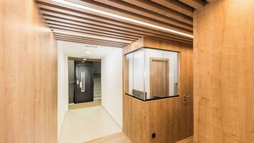 Een hal met houten wanden en plafond, een glazen lift en een deur naar een andere kamer.