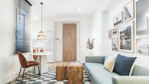 Een ruimtelijke woonkamer met een bank, een eettafel met stoelen, een bijzettafeltje, een hanglamp en een muur met ingelijste foto’s.