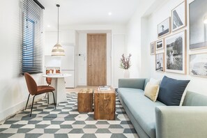 Un espacio habitable compacto con sofá, una mesa de comedor con sillas, una mesa de centro, una lámpara colgante y una pared decorada con cuadros.