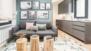 A modern living room with a grey sofa, a coffee table, and a kitchen area with grey cabinets and a window. - Doctor Castelo XL - One Bedroom Apartment, Sleeps 2 (Madrid)