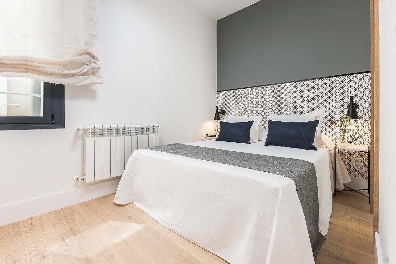 Een moderne slaapkamer met een bed, nachtkastjes, een radiator en een raam met gordijnen.