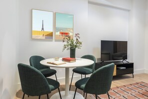 Ein modernes Wohnzimmer mit einem runden Tisch, vier Stühlen, einem Fernseher und Kunstwerken an der Wand.