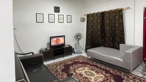 Un salon avec un canapé, un téléviseur, un ventilateur et un tapis à motifs.