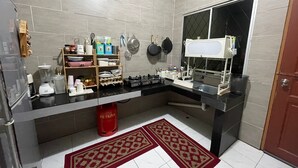 Une cuisine moderne avec des murs recouverts de carreaux gris, un plan de travail noir et une fenêtre. On y trouve divers ustensiles et appareils de cuisine, notamment un mixeur, une bouilloire et une cuisinière à gaz. Une poubelle rouge est visible sous le plan de travail.